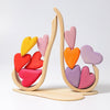 A Grimm's Red Hearts Building Blocks with a natural finish is stacked with colorful heart-shaped blocks in shades of yellow, red, pink, and purple. The hearts are arranged in a symmetrical, cascading pattern, creating a playful and aesthetically pleasing design that enhances fine motor skills.