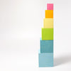 A Grimm's Large Pastel Set of Boxes featuring a vertical stack of colorful, non-toxic wooden blocks of varying sizes is arranged in descending order. The blocks, starting from the bottom to top, are light blue, blue, green, yellow, orange, and pink against a white background. Perfect for stack and sort activities.