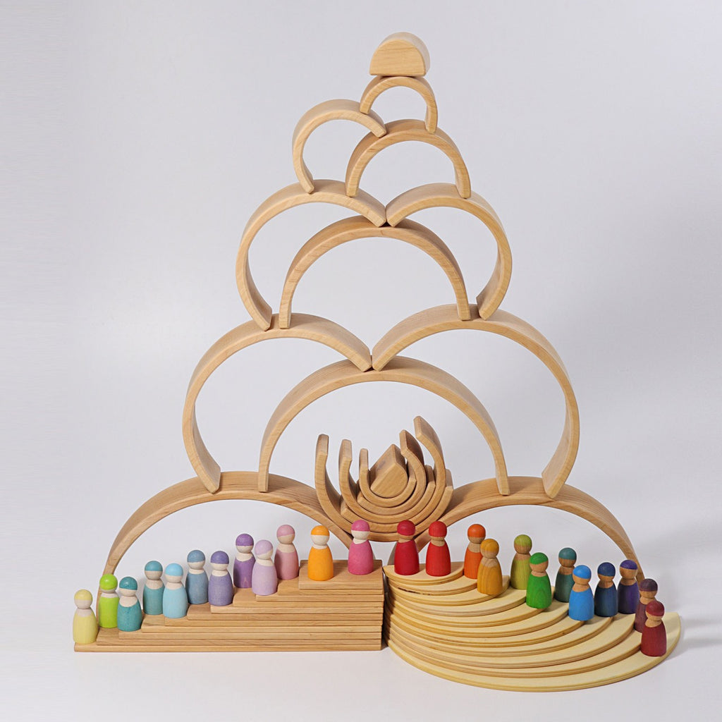 A Grimm's Large Natural Rainbow Stacker arranged into a pyramid shape with multiple layers. Below the pyramid, small wooden peg dolls painted in various colors are lined up in two rows, forming a semicircle and a straight line, giving an organized and colorful display reminiscent of a Natural Tunnel.