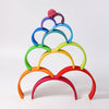 A vibrant and whimsical Grimm's Large Wooden Rainbow displayed in a pyramid arrangement. Each arch, handcrafted from non-toxic wood, features vivid colors: red, orange, yellow, green, blue, purple, and pink. This versatile toy adds a visually appealing touch against a white background.