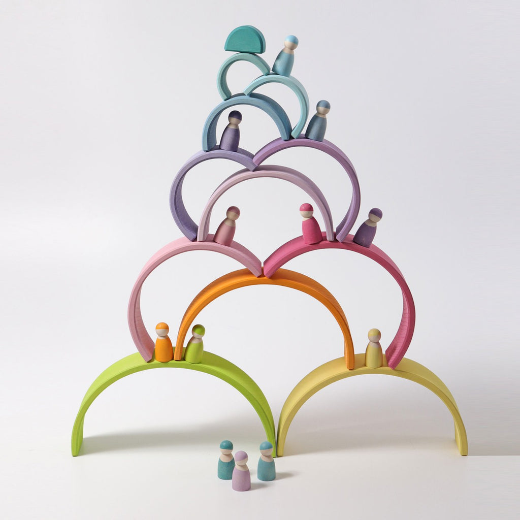 A balanced pyramid of colorful, non-toxic wooden arches topped with small wooden peg dolls in matching hues. This versatile stacking Large Wooden Rainbow, Pastel is arranged in a visually harmonious pattern, with bright colors including green, orange, purple, pink, and blue against a white background.