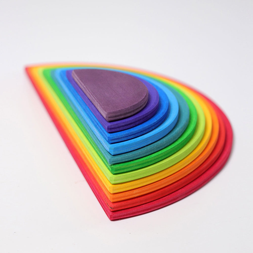 The Grimm's Rainbow Semi Circle Set features a beautifully crafted stack of wooden shapes, each painted in a vibrant rainbow color from red on the outside to purple in the center, arranged in descending size order. Little architects will adore this extra large creative puzzle, perfectly aligned on a white background.