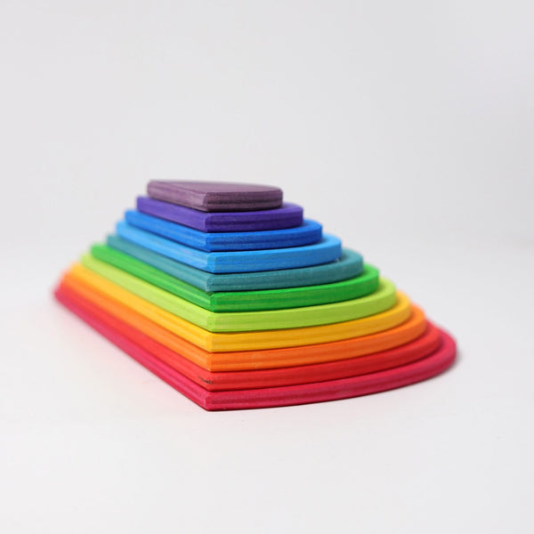 A stack of colorful, semi-circular shapes from Grimm's Rainbow Semi Circle Set, arranged in incremental sizes with the largest at the bottom and the smallest at the top, forming a vibrant rainbow-like gradient from red to purple. This extra-large creative puzzle is perfect for little architects exploring versatile modern architecture against a plain, white background.