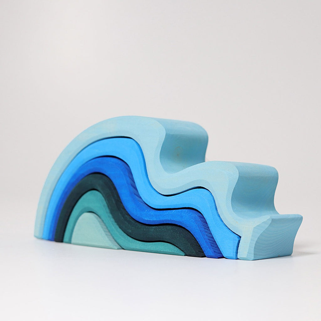 Introducing Grimm's Ocean Waves: a beautifully crafted wooden puzzle shaped like a waterwave, made from lime wood. This versatile toy showcases pieces stacked in shades of blue and teal, creating a stunning gradient effect. Its design is simple and abstract, featuring smooth curves and a minimalist appearance.