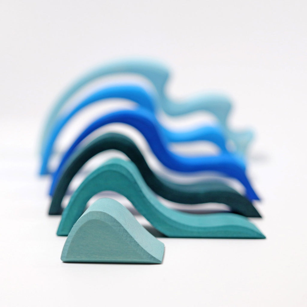 A set of Grimm's Ocean Waves, featuring abstract waterwave shapes in blue and teal, crafted from lime wood, is arranged from smallest to largest against a white background.