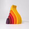 The Grimm's Fire Stacker consists of colorful, curved wooden pieces primarily in shades of yellow, orange, and red, arranged in an abstract, branching pattern against a white background. This charming wooden stacking toy also features a small purple piece shaped like a truncated cone placed in the foreground.