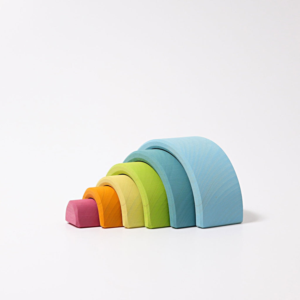 A versatile toy featuring a set of colorful wooden rainbow stacking arches arranged in a gradient. Crafted from lime wood, the smallest arch is red, followed by orange, yellow, light green, dark green, and the largest arch is blue. The arches are stacked neatly from smallest to largest on a white background. 

Introducing Grimm's Small Wooden Rainbow, Pastel!