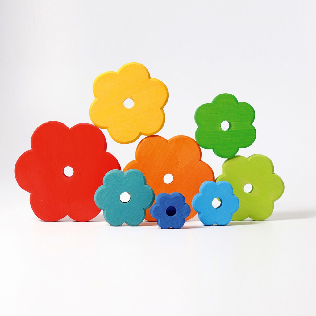 Introducing Grimm's Flower Stacking Tower: a vibrant children's stacking toy featuring a blue central peg. The non-toxic pieces come in various colors and sizes, from small blue and green flowers to larger red, orange, and yellow blooms. Each flower boasts multiple holes that encourage the development of fine motor skills as they are arranged around the peg.