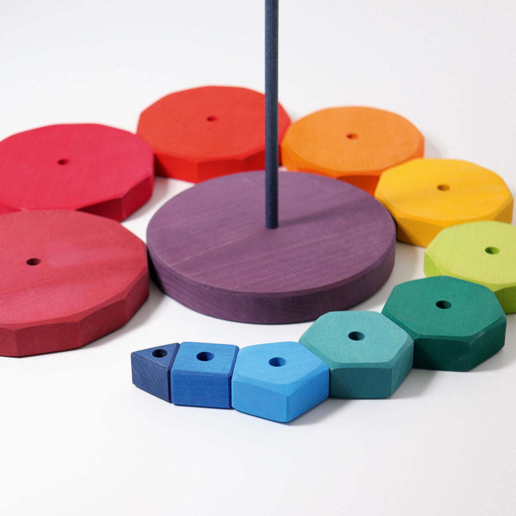 A colorful wooden stacking toy with various flat, polygonal shapes in different sizes and colors arranged around a central vertical rod. This non-toxic Grimm's Giant Geometrical Stacking Tower features pieces ranging in hues from red and purple to blue, green, and yellow, perfect for enhancing fine motor skills.