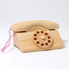 Introducing the Grimm's Wooden Telephone, a non-toxic toy shaped in a simple, old-fashioned design. It features a wooden rotary dial and a pink string attached to the handset, all set against a plain white background.