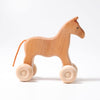 A Grimm's Wooden Horse Willy Push Toy with a simple design, featuring four round wheels and a rope tail. Made in Germany, this push toy is crafted from light-colored wood and stands against a plain white background.