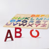 The Grimm's ABC Game, a wooden alphabet puzzle featuring vibrant letters made from non-toxic materials, is displayed on a white background. The letters A, B, and an upright O are removed and positioned in front of the puzzle. The remaining letters rest snugly in their designated slots within the wooden frame.