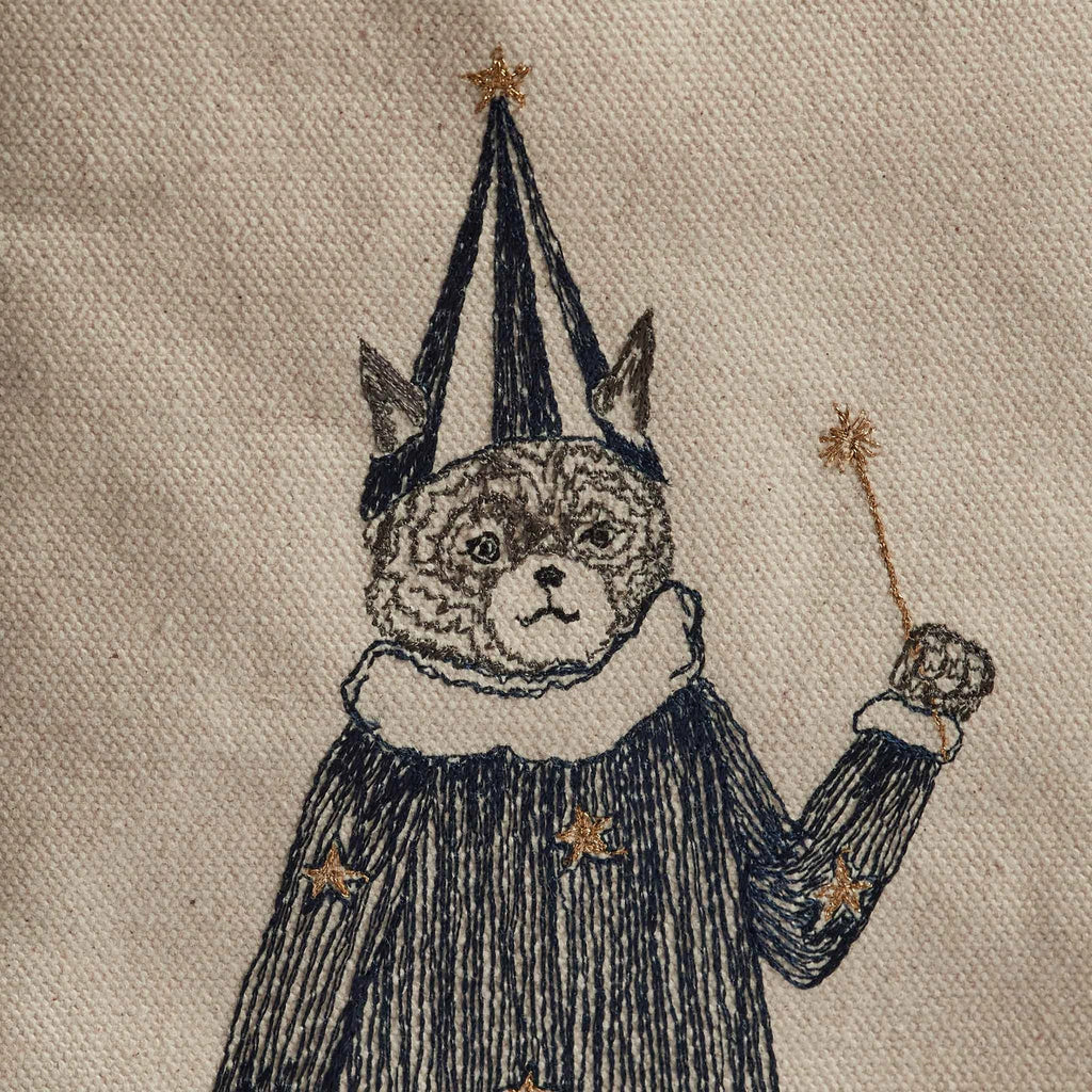 Illustration of a cat dressed as a wizard, featured on the Coral & Tusk Halloween Costumes Bag. The costumed critter wears a patterned robe with stars, a pointed hat, and holds a wand with a sparkling tip. The background consists of a textured, light-colored canvas perfect for trick-or-treat fun.