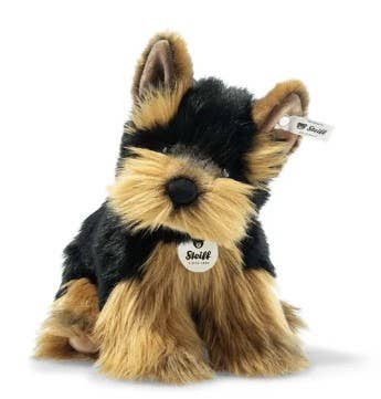 Introducing the Steiff Yorkshire Terrier Plush Toy Dog, a charming toy that perfectly captures the essence of everyone's favorite tiny pup. With black and tan fur, upright ears, an adorable snout, and featuring a tag on one ear alongside a label on its chest, this plush toy delightful resembles a Yorkshire Terrier.