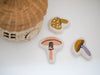 Three Mini Mushroom Baskets in different colors next to a hand-woven basket on a white surface.