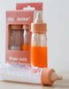 A pair of baby bottles, with one containing orange liquid and the other clear, are positioned in front of a pink package labeled "Bottled milk and juice set - Tiny Harlow." These bottles are ideal for enhancing doll feeding experiences. The softly blurred background accentuates the beauty of both the bottles and their packaging.