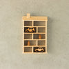 A Wooden Shelf No. 22 shaped like a house with a chimney is mounted on a grey wall in the children's room. The kids' storage shelves feature multiple compartments, housing two wooden toy cars and two wooden toy trees, all neatly arranged on different levels.