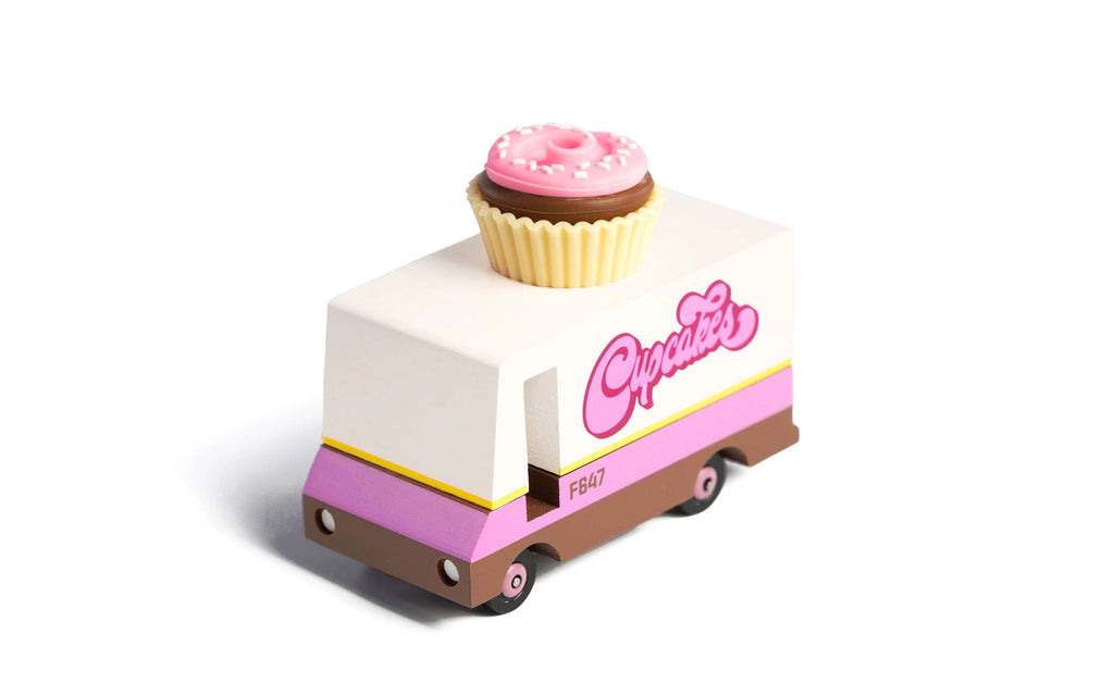 A Candylab Mini Food Truck designed with pastel colors, featuring "Cupcakes" written in pink on the side. The top of the truck has a whimsical cupcake and donut decoration, adding a playful touch. The adorable donut truck has small wheels and is stylized with a cute, chunky form.