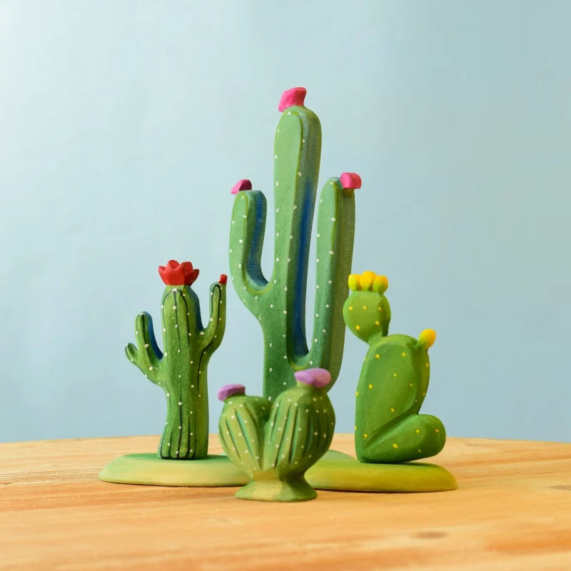 The Bumbu Wooden Cacti Set showcases a colorful clay representation of various cacti on a light wood surface with a light blue background. This eco-friendly set features brightly colored flowers in shades of pink, red, and yellow, adding a cheerful touch to the scene and making it perfect for imaginative play.