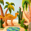 The Bumbu Wooden Cacti Set by Bumbu Toys features a colorful, wooden diorama with two camels amidst charming cacti and palm trees. The scene includes a small pond with blue water-like patterns and sand-like terrain, depicting a desert oasis setting. Bright and cheerful, it has a playful, handcrafted look.