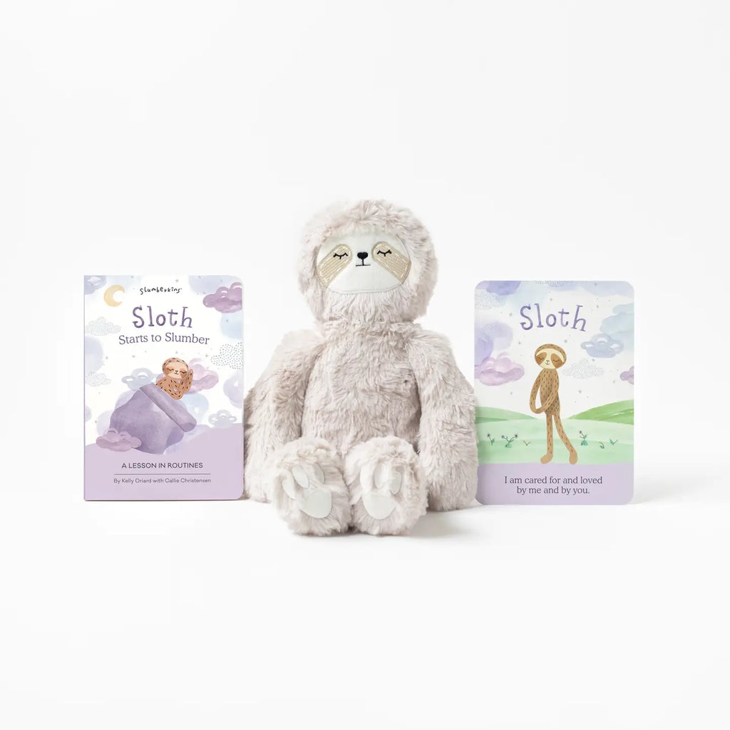 A plush Slumberkins Sloth Kin toy is placed between two illustrated children's books titled "Starts to Slumber" and "Sloth." The scene is simple, with a white background emphasizing these relaxing sloth-themed items.