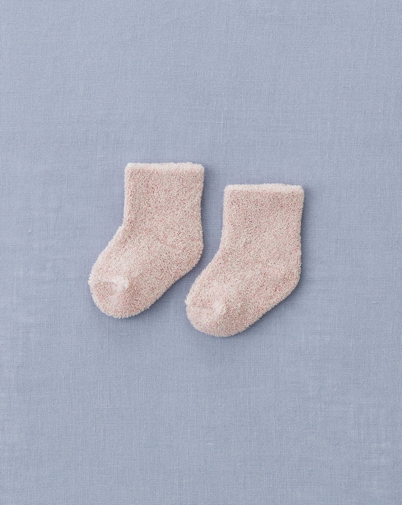 A pair of Baby Pile Knit Socks - Pink is placed side by side on a light blue textured fabric surface.