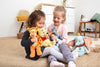 Two young girls sit on a beige carpet, grinning as they play with plush toys, including a 12-inch Steiff Disney's Tigger the Tiger stuffed plush toy, alongside Winnie the Pooh and Dumbo, in a cozy room with a chest of drawers in the background.