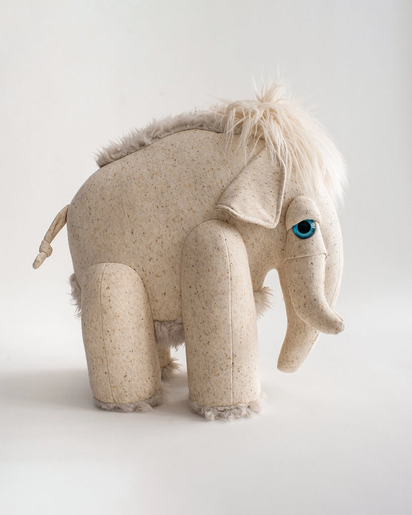 A plush toy resembling an elephant with light beige, speckled fabric, a short tail, shaggy fur on its back and head, and blue eyes. Standing on a plain white background, this BigStuffed Albino Mammoth Stuffed Animal has a unique charm reminiscent of an Albino Mammoth plush.