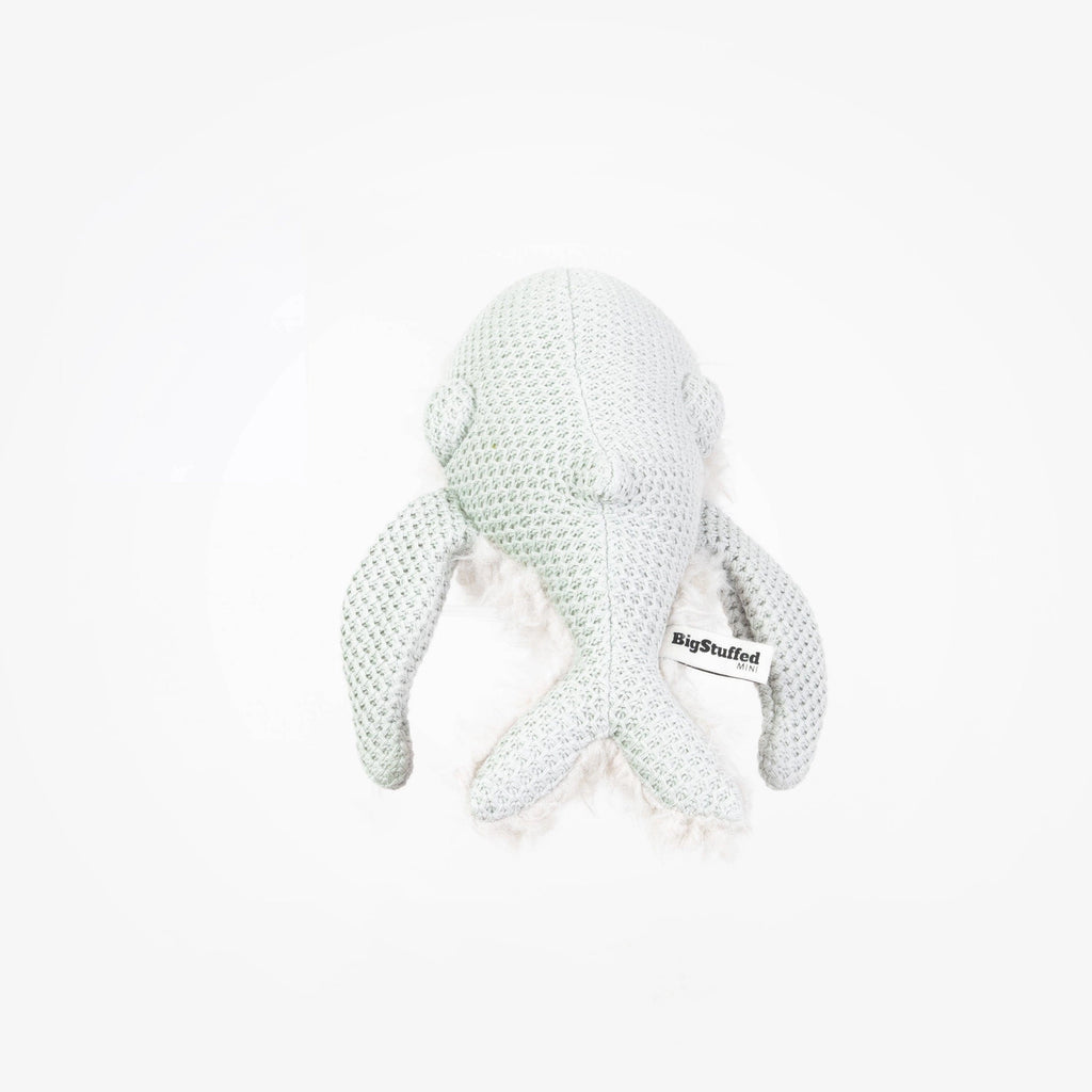 A soft, white, knitted stuffed animal resembling a marine creature, possibly a whale, shown from the back. Handcrafted and made in Lithuania, it features a tag labeled "BigStuffed" attached to its side. The background is plain and white.