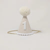 Introducing the White Party Hat: a charming accessory perfect for birthday celebrations. This small, light beige hat features a large white pom-pom on top and is adorned with the number "1" in white on the front. It also boasts a white trim at the base and includes an elastic strap for comfortable wearing. The hat is set against a plain white background, making it an ideal choice for commemorating special occasions.