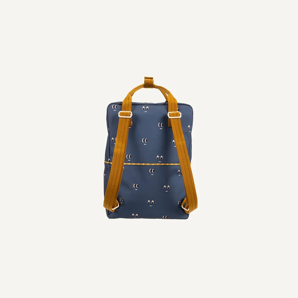 The Sticky Lemon Backpack Large | Special Edition Eyes in Boxing Blue is a square-shaped, navy blue backpack adorned with a pattern of small, white crescent moons. Made from recycled PET bottles, it features mustard yellow shoulder straps and a top handle. Enhanced with waterproof lining, it sits against a plain off-white background.