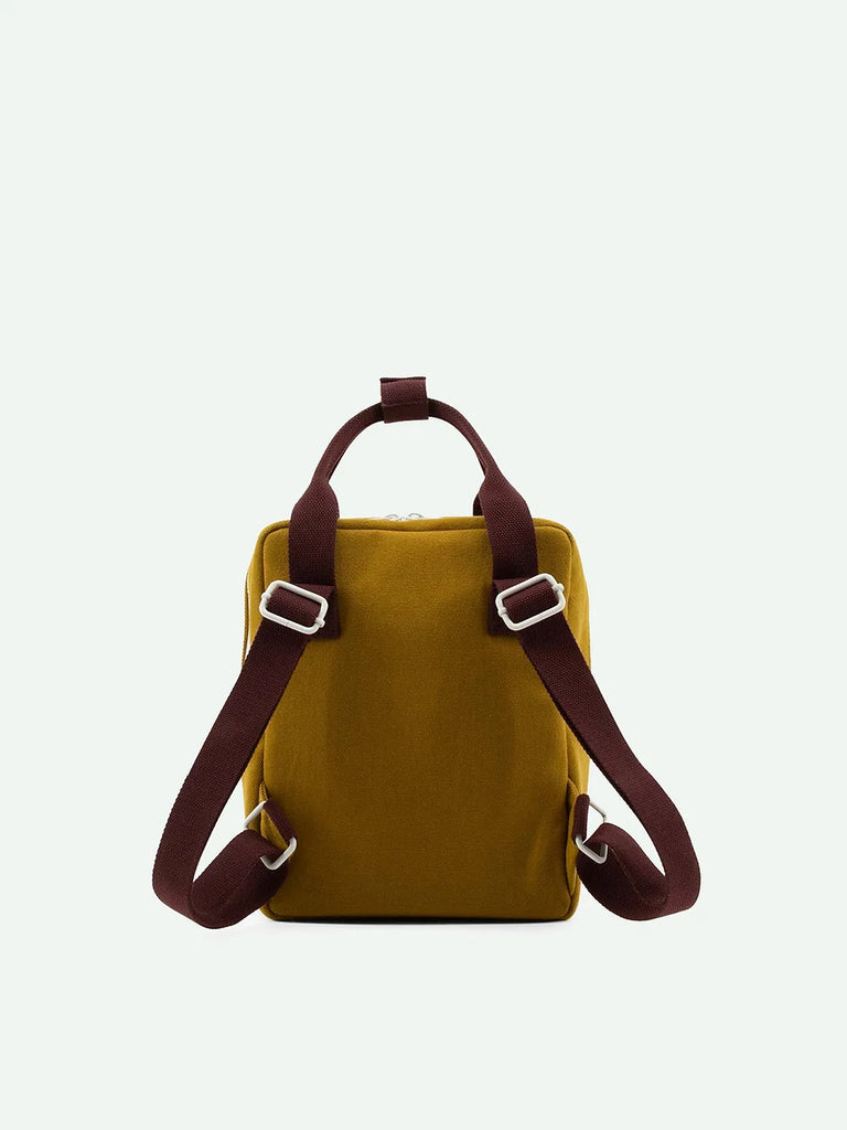 A small, square-shaped khaki green Sticky Lemon Backpack Small Special Edition from the Adventure Collection made from waterproof nylon, featuring dark brown adjustable shoulder straps and a matching top handle. The front of the backpack is plain, and the background is a light off-white color.