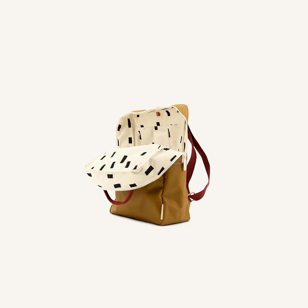 A stylish Sticky Lemon backpack with a dalmatian print flap and burgundy straps, featuring a waterproof nylon body, positioned upright against a plain, light background.