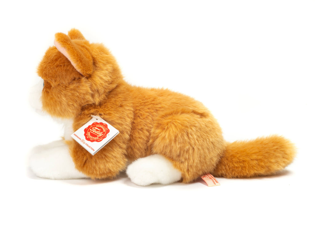 The Teddy Hermann Orange Laying Cat Stuffed Animal is a high-quality plush toy with soft and fluffy orange and white fur, lying on its belly with its front paws extended forward. A red and white tag displaying the Hermann Teddy Collection logo and text is attached to its neck.