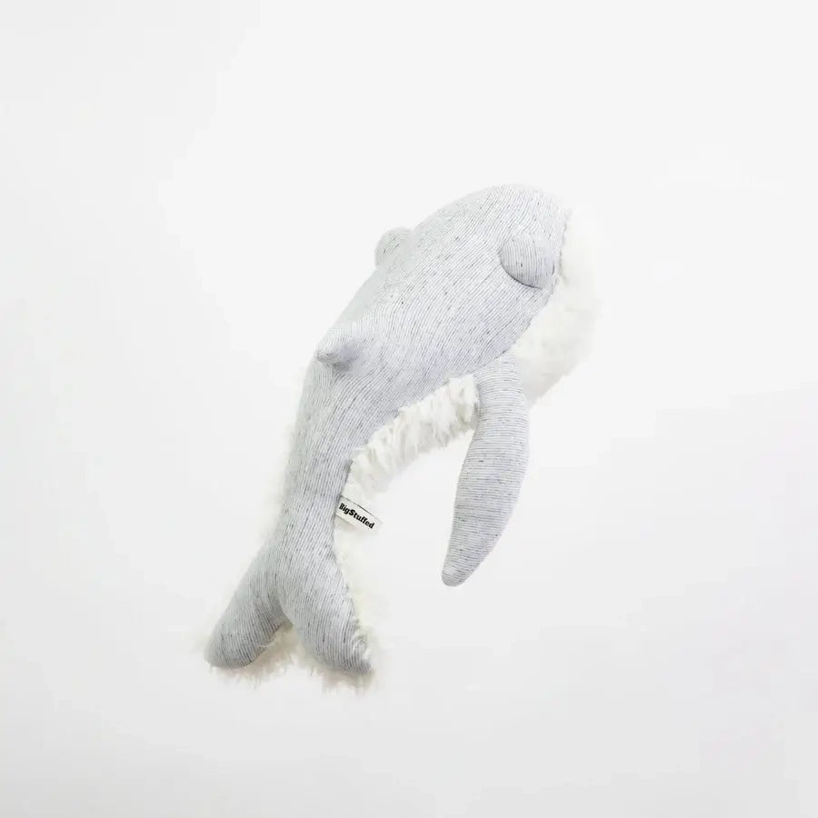 The BigStuffed Small Grandpa Whale is a soft, light gray plush toy with a minimalist design, featuring two flippers and a small fin on top. Resting against a plain white background, this cuddly toy is made of fuzzy fabric, giving it a cozy appearance that is perfect for hugs and cuddles.