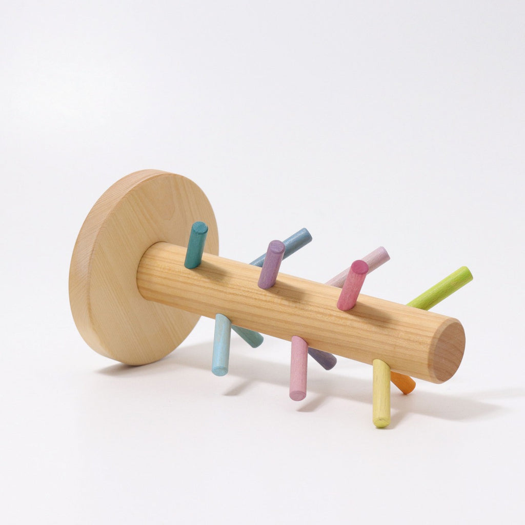 The Grimm's Pastel Sorting Helper for Building Rings is a wooden toy crafted from alder-wood, featuring a cylindrical base with a flat circular end. Several small, colorful pegs, painted in non-toxic pastel shades of blue, pink, green, and yellow, protrude at various angles. The toy is displayed against a plain white background.