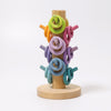 The Grimm's Pastel Sorting Helper for Building Rings is a non-toxic wooden toy crafted from alder-wood, featuring a vertical cylindrical column on a round base. It is adorned with colorful Building Rings looped on shorter horizontal pegs of the same hue and vibrantly showcases shades of green, orange, pink, purple, and blue arranged from top to bottom.