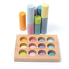 A Grimm's Stacking Game Small Pastel Rollers with a rectangular base featuring 12 circular slots, each painted a different pastel color. Twelve matching pastel-colored cylinders are arranged next to the base, with some stacked on top of each other. This engaging toy aids in developing motor skills and color sorting abilities.
