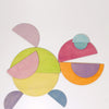 A collection of colorful wooden shapes arranged on a white background. The pieces include circles, semi-circles, and other geometric shapes in various pastel hues such as yellow, pink, green, blue, and purple. This Pastel Semi Circle Set forms an abstract pattern reminiscent of modern architecture.