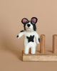 A small, needle-felted French Bull Dog Finger Puppet in black and white, with pink inner ears, stands on a wooden base. Crafted from 100% wool, the dog has one paw raised against a plain light brown background.