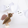 A crafted scene features a single brown, textured paper bird with wings mounted and standing on a flat surface. Above it, two Meri Meri Honeycomb Owls in white, complete with round eyes and outspread wings, hang from the ceiling—perfect for Halloween decorations. The background is plain and white.