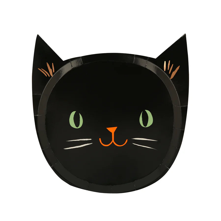 The Meri Meri It's Halloween! Plates are black paper plates designed to resemble a cat's face, perfect for Halloween. They feature green eyes, an orange nose and mouth, whiskers, and pointed ears with orange inner ear details. The background is plain white.