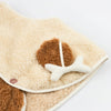 A close-up of the Meri Meri Puppy Costume - Final Sale reveals fluffy beige and brown sherpa fleece fabric adorned with a button and a small bone-shaped plush attachment. The texture is soft and fuzzy, making it perfect for any dog lover gift or as an adorable puppy costume for children.