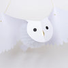 The Meri Meri Honeycomb Owl is a hanging white paper decoration featuring an owl with wide, spread wings. The owl has striking black round eyes, a simple gold beak, and intricate paper folds that form its body, giving it a three-dimensional appearance. This enchanting party decoration stands out beautifully against the plain white background.