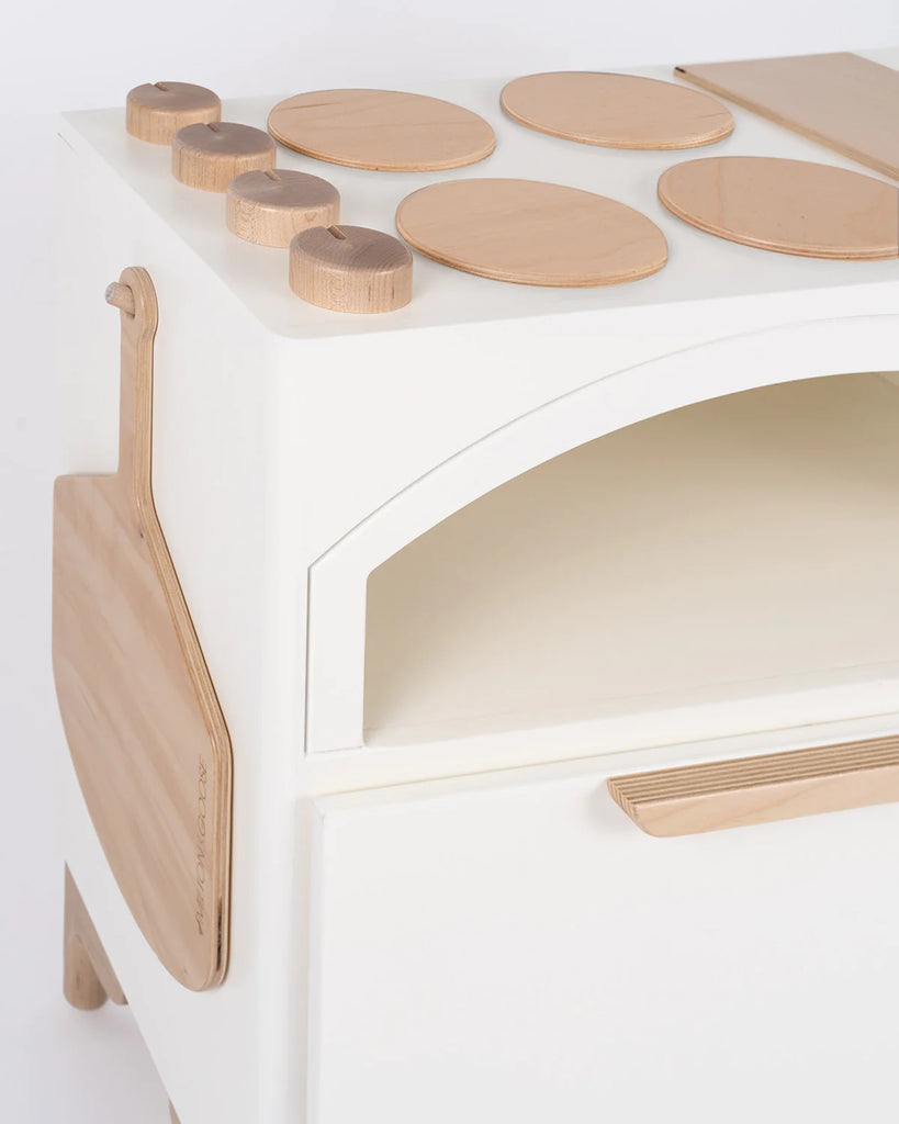 A modern white wooden Milton & Goose Play Kitchen With Pizza Oven - Made in USA partially visible in the frame, featuring a curved design with natural wood accents. The top has assorted oval and circular wood plates, and represents an interactive educational toy.