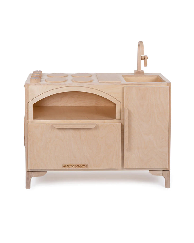 A Milton & Goose Play Kitchen With Pizza Oven featuring a stove, oven, sink, and storage compartments, made from light-colored wood, with a simple, minimalistic design. This interactive educational toy encourages imaginative play and learning.