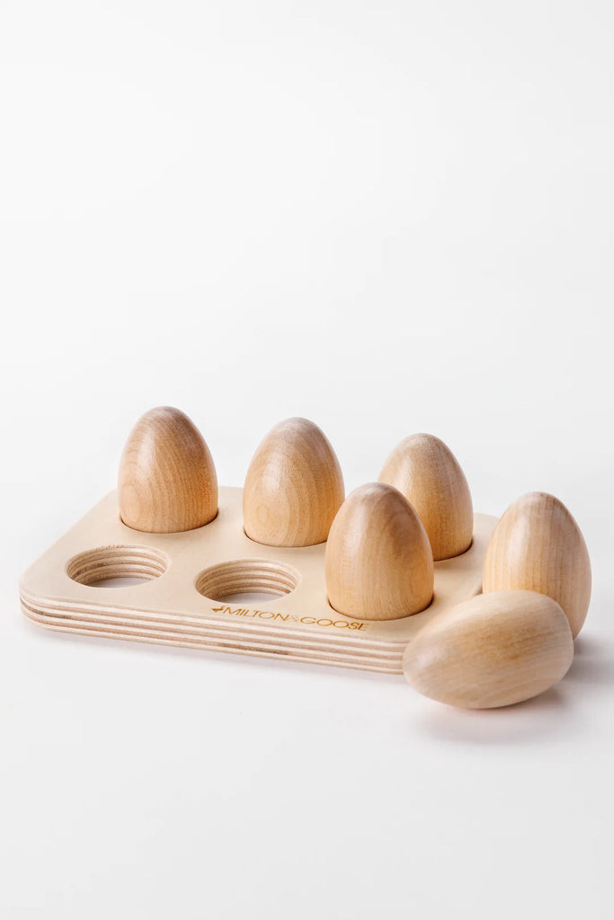 A wooden board featuring six slots, each holding a Milton & Goose Wooden Half Dozen Egg from Amish crafted toys. The board and eggs have a smooth, light wooden finish, set against a plain white background.