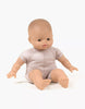 The Minikane Soft Body Doll (11") - Jasper, dressed in a light pink short-sleeved onesie, sits with legs spread and arms slightly extended. Crafted from phthalate-free vinyl, the doll features bald, pale plastic skin and small details, set against a plain white background—making it an ideal bedtime companion.