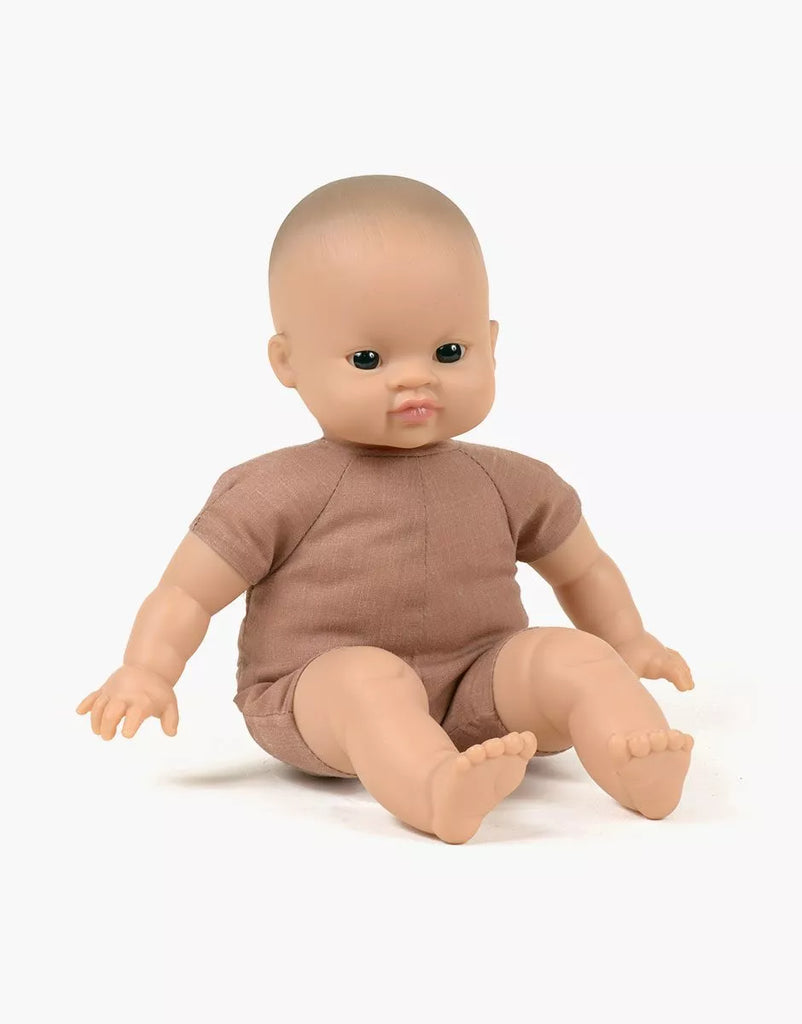 A bald, light-skinned Minikane Soft Body Doll (11") - Matteo with a neutral expression is seated on a white background. The doll, crafted from phthalate-free vinyl and wearing a short-sleeved brown romper, features detailed fingers and toes. This charming doll makes an ideal bedtime companion.