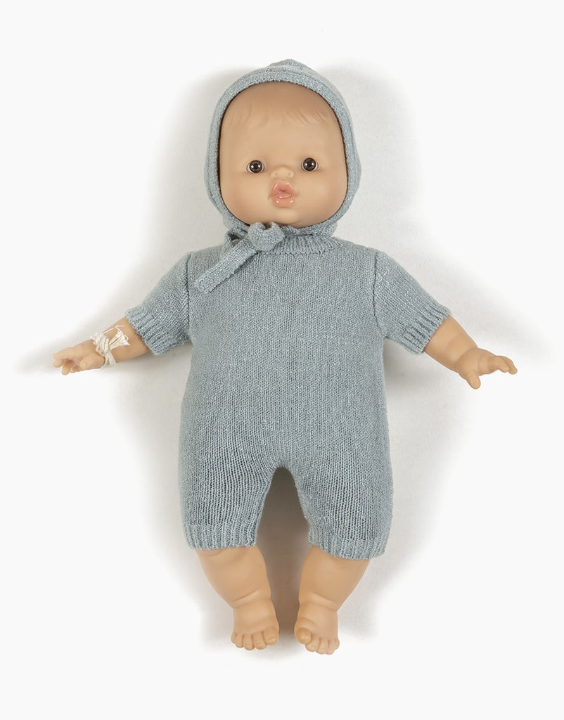 A Minikane Doll Clothing | Élie Blue Knit Bonnet is dressed in a light blue, knitted crush onesie with short sleeves and a matching bonnet. With a light complexion and open eyes, Élie is positioned upright with arms and legs slightly spread apart against a white background.